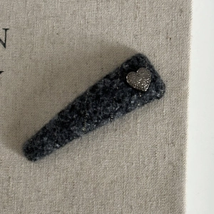 Close-up of a charcoal wool hair clip featuring a textured silver metal heart on top
