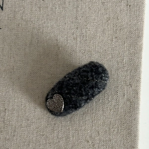 Close-up of a dark grey felt hair clip with golden stitching and a silver heart accent
