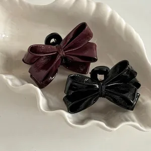 Glossy leather bow hair claw clips in burgundy and black set on decorative ceramic plate