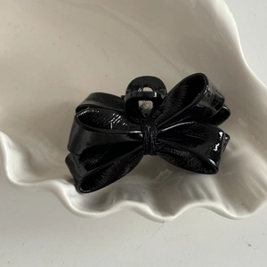 Glossy black patent leather bow hair claw clip for women on a white ceramic plate