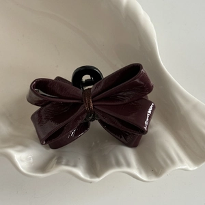 Macro shot of glossy burgundy faux leather mini bow hair claw on white shell tray