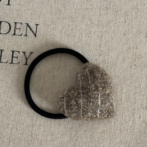 Close-up of heart-shaped brown tweed hair tie with gold thread on linen fabric