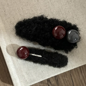 Dettaglio di fermagli per capelli in peluche con perline bordeaux e grigie su tessuto