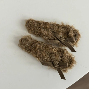 Close-up of two brown plush bow hair clips featuring soft curly faux fur textures