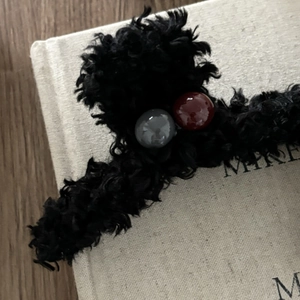 Dettaglio di un fermaglio per capelli in peluche nero con perline grigie e rosso scuro