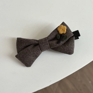 Detail of dark brown wool bow hair clip with yellow floral embroidery and metal duckbill clip
