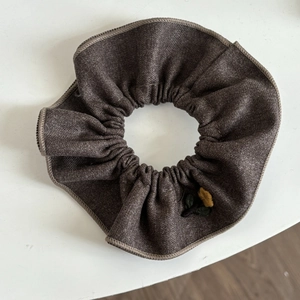 Detailed shot of dark brown wool scrunchie with yellow floral embroidery and fine stitching