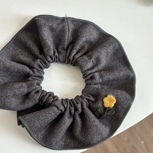 Detail of dark gray scrunchie with yellow floral embroidery and reinforced stitched edges