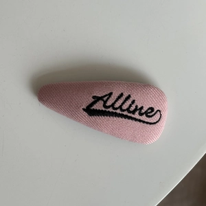 Dettaglio di un fermaglio per capelli in tessuto rosa con ricamo Alline in corsivo