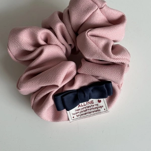 Dettaglio di scrunchie rosa a righe con fiocco blu scuro ed etichetta in tessuto