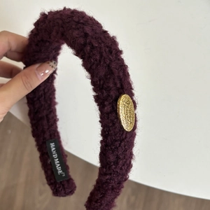 Detail des weinroten Lammwoll-Stirnbandes mit goldenem Metalletikett und Handmade-Label