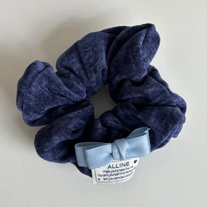Dettaglio di uno scrunchie blu scuro a righe con un fiocco azzurro ed etichetta tessuta