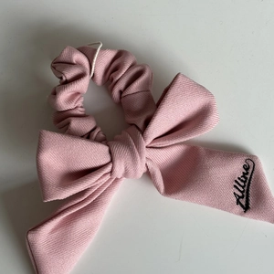 Dettaglio dell'elastico per capelli con fiocco rosa, trama a saia e ricamo in corsivo nero