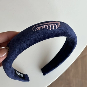 Dettaglio di un cerchietto in velluto blu scuro con elegante ricamo Allure rosa e consistenza