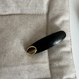 Detail of a black leather oval hair clip featuring a gold metal PARIS engraved plate