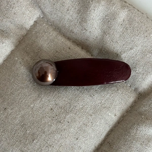 Macro detail of dark brown faux leather hair clip with a vintage metallic pearl ornament