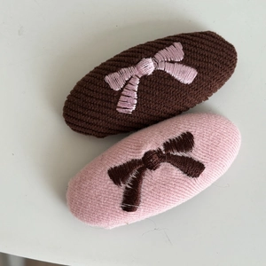 Detail of two knit bow hair clips featuring delicate pink and brown embroidery for women