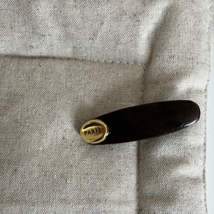 Deep brown leather hair clip with gold Paris metal inlay on beige fabric background
