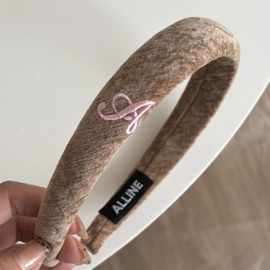 Close-up of brown velvet headband with pink embroidered letter A and brand label