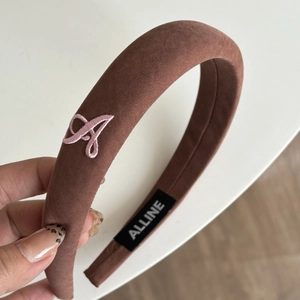 Detail of a brown plaid headband with pink embroidered letter A and high-quality texture