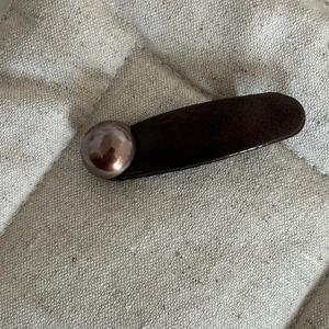 Detail of dark brown leather hair clip with bronze spherical accent on textured fabric