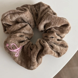 Detailed view of brown corduroy scrunchie with elegant pink embroidered lettering