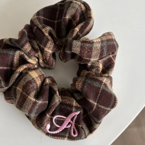 Detailed view of a brown plaid scrunchie featuring a pink embroidered letter A