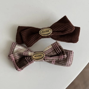 Close-up of brown corduroy and pink plaid bow hair clips with golden oval metal buckles
