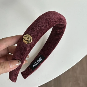 Detail view of burgundy velvet headband featuring a circular gold metal logo ornament
