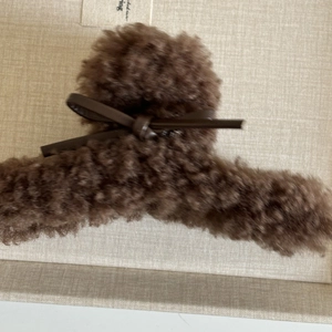 Gros plan d'une pince à cheveux en peluche marron avec un nœud en cuir sur fond de tissu