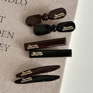 Brown and black resin hair clip set with gold lettering on elegant linen background