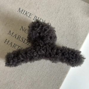Détail d'une pince à cheveux en peluche gris anthracite sur un fond de livre élégant