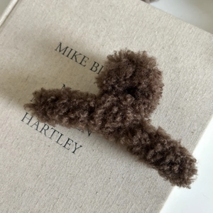 Vue détaillée d'une pince à cheveux en peluche marron café sur un fond de livre
