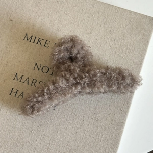 Gros plan sur une pince à cheveux marron en peluche bouclée sur fond en lin
