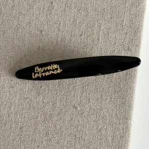 Detailed view of black resin barrette with gold logo on soft fabric background