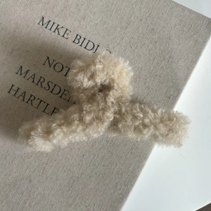 Gros plan d'une pince à cheveux en peluche beige sur un fond en tissu texturé