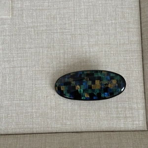 Detailed macro view of an oval hair clip with blue and green mosaic pixel patterns