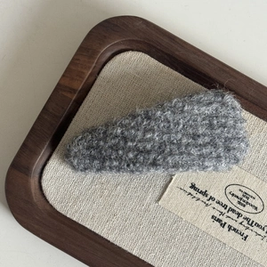 Detailed close-up of grey plush faux fur BB hair clip on a minimalist wooden display