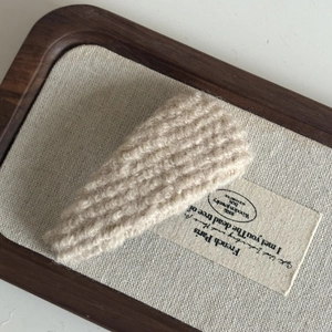 Detail of cream cable-knit hair clip showing texture and weave on a linen display tray