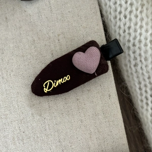 Detail of pink heart-shaped corduroy hair clip with golden metal Dimoo letter logo