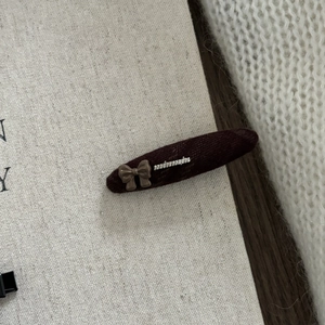 Macro shot of a dark brown velvet hair clip with light brown bow and silver letters