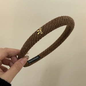 Detailed macro view of dark brown knitted headband with a gold bow and handmade label