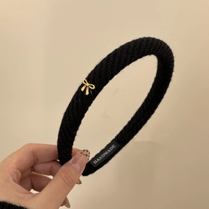 Detail view of black twill fabric headband with small golden metal bow and handmade label