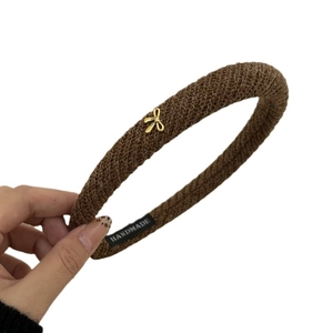 Minimalist dark brown knitted headband with a spiral twist pattern and gold bow charm