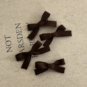 Detailed set of four dark brown velvet bow hair clips on a textured beige fabric background