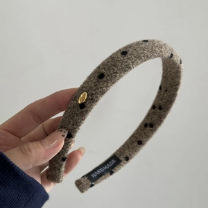 Detail of wool fabric headband with black polka dots and gold-tone metal plate engraving