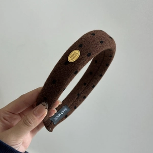 Détail d'un serre-tête en laine marron à pois avec logo doré et étiquette fait main