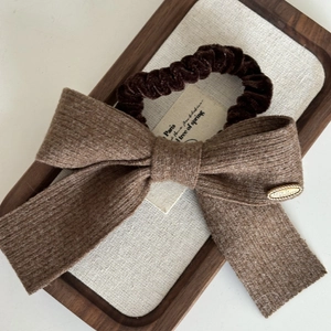 Close-up of brown bow hair scrunchie with knit texture and Love is Forever metal tag