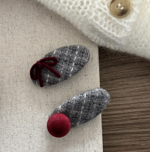 Close-up of grey tweed hair clips with burgundy velvet bows on a warm knitted background