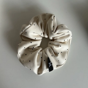 Detailed close-up of cream scrunchie with black polka dots and a bow logo tag